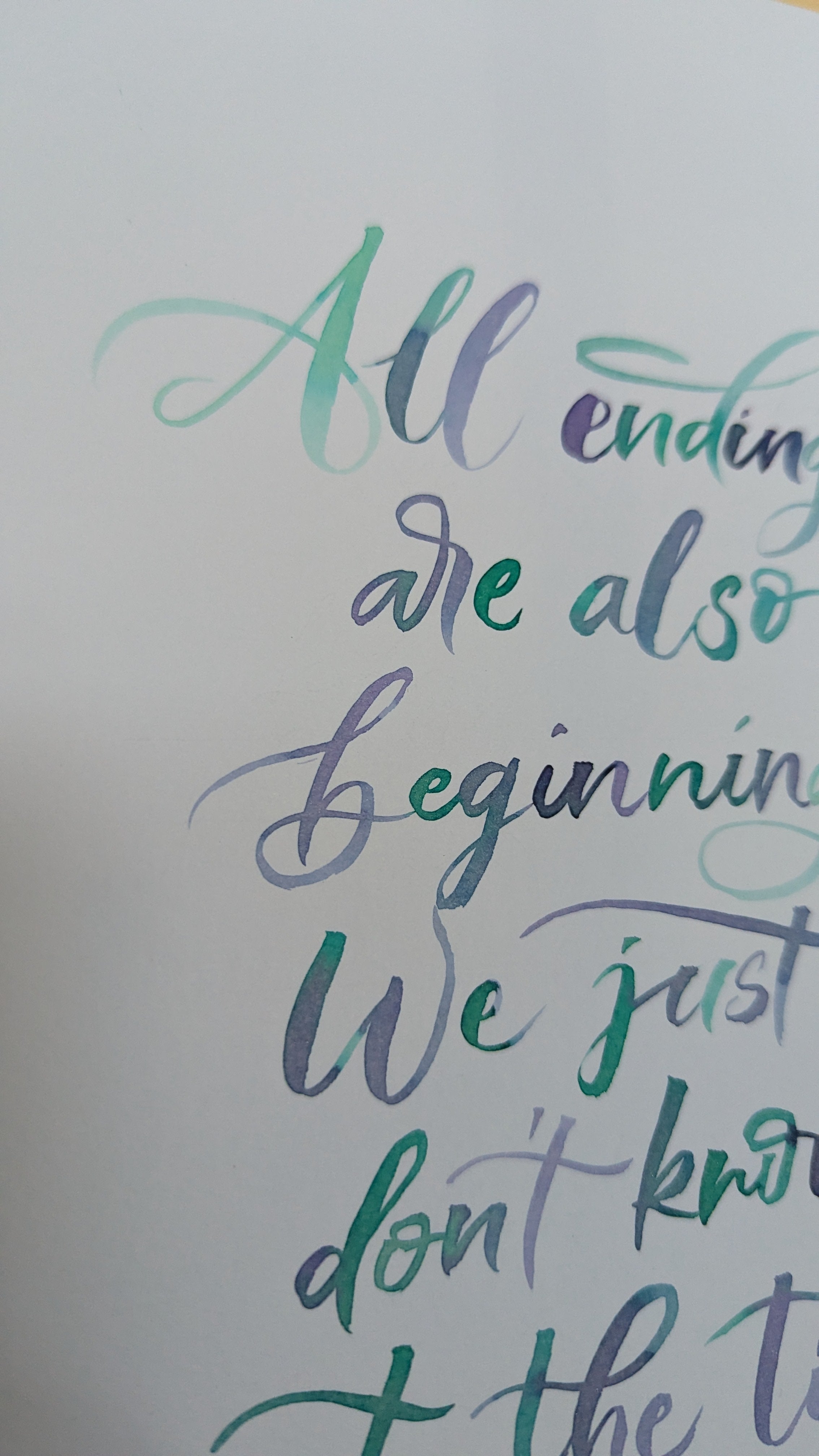 Close-up of a hand-lettered quote on a white background, with the visible text reading 'All endings are also beginnings. We just don't know the time.