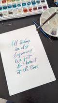 A white sheet of paper with colorful calligraphy text reading 'All endings are also beginnings. We just don't know it at the time.