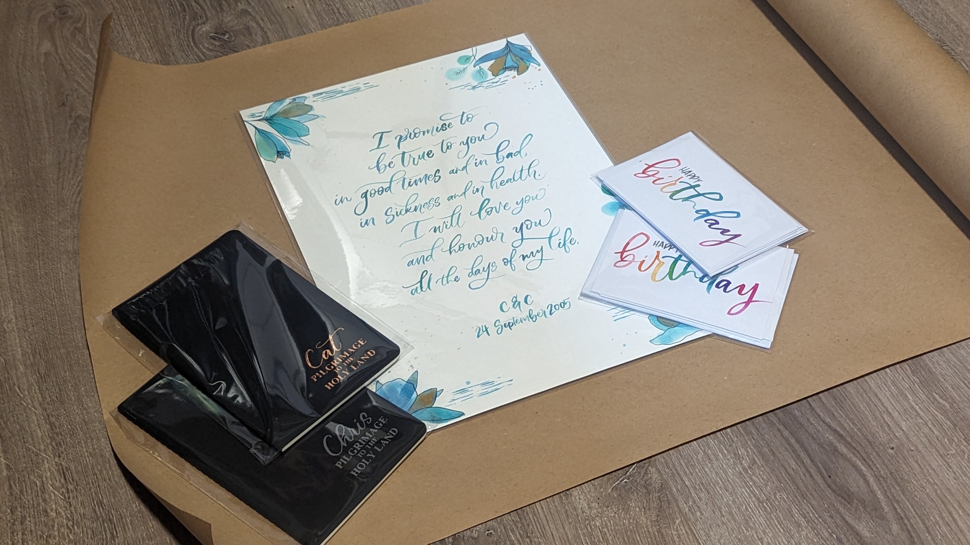 A flat-lay of a custom wedding invitation suite on a brown kraft paper background. The set includes a main invitation card with elegant blue calligraphy and floral accents, two matching RSVP cards with colorful 'birthday' script, and two black foil-engraved wedding save-the-dates.