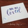Original, hand-painted brush-lettered artwork of the words “You are loved” on 300GSM acid-free watercolour paper with high-quality Ecoline ink in dark blue and purple. All designs are copyrighted © Joy Adan 2018.