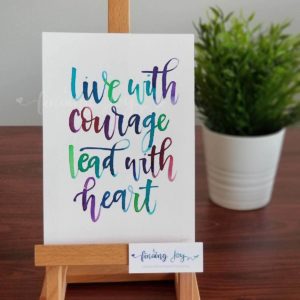 Original, hand-painted brush-lettered artwork of the words "Live with courage, lead with heart" on A5 300GSM card in green, blue, violet and maroon watercolour ink. All designs are copyrighted © Joy Adan 2018.