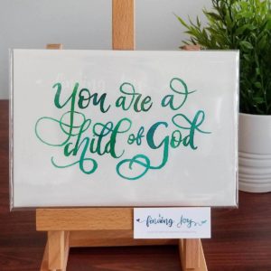 Original, hand-painted brush-lettered artwork of the words "You are a child of God" on A5 300GSM card in green watercolour ink.