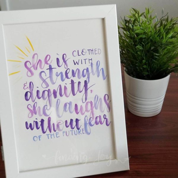 Original, hand-painted brush-lettered artwork of Proverbs 31:25 written in purple watercolour paint on A4 300GSM card.