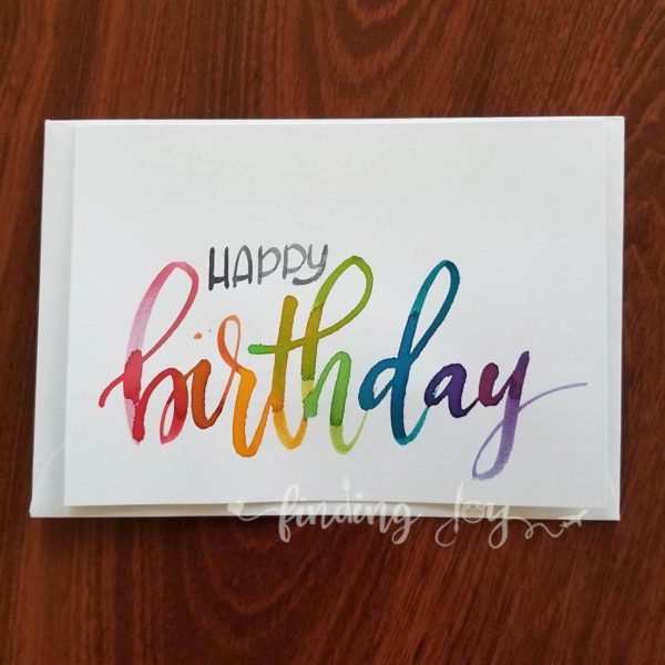 Hand-painted greeting card with 'Happy birthday' hand-lettered in multicolour/rainbow Ecoline ink. Each card is lettered on matte card stock. Inside: blank. © Joy Adan 2018