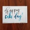 "Happy Cake Day" Greeting Card written in watercolour brush calligraphy in black and blue © Joy Adan