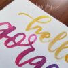 Greeting card with "hello gorgeous" hand-lettered in gold and fuschia Ecoline ink. Each card is painted on matte card stock. Inside: blank. © Joy Adan 2018
