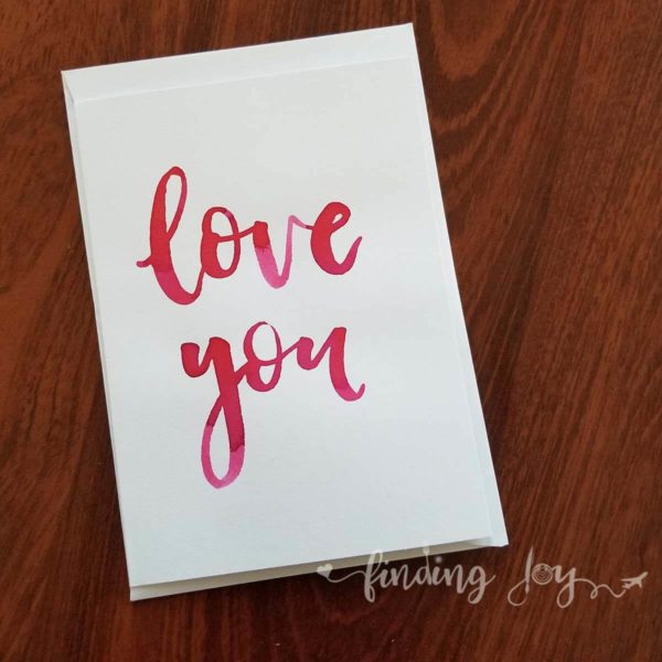 Greeting card with 'love you' hand-lettered in fuschia Ecoline ink. © Joy Adan